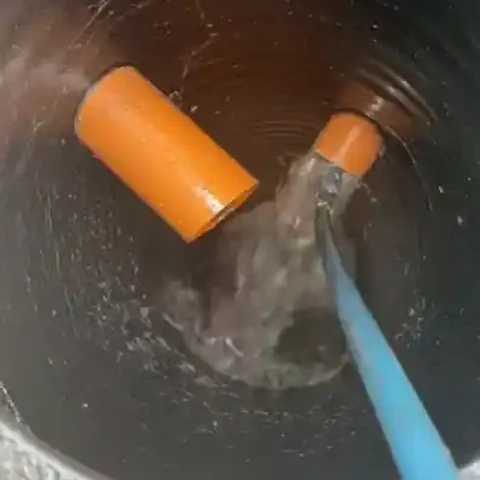 Outdoor drain after cleaning Round drain basin with water flowing from a blue hose after clearing a clogged drain